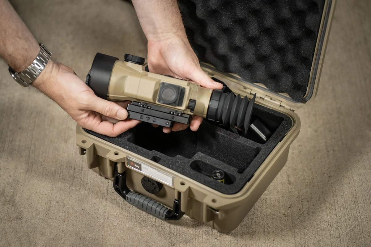 Hands unboxing thermal scope from protective hard case on concrete surface