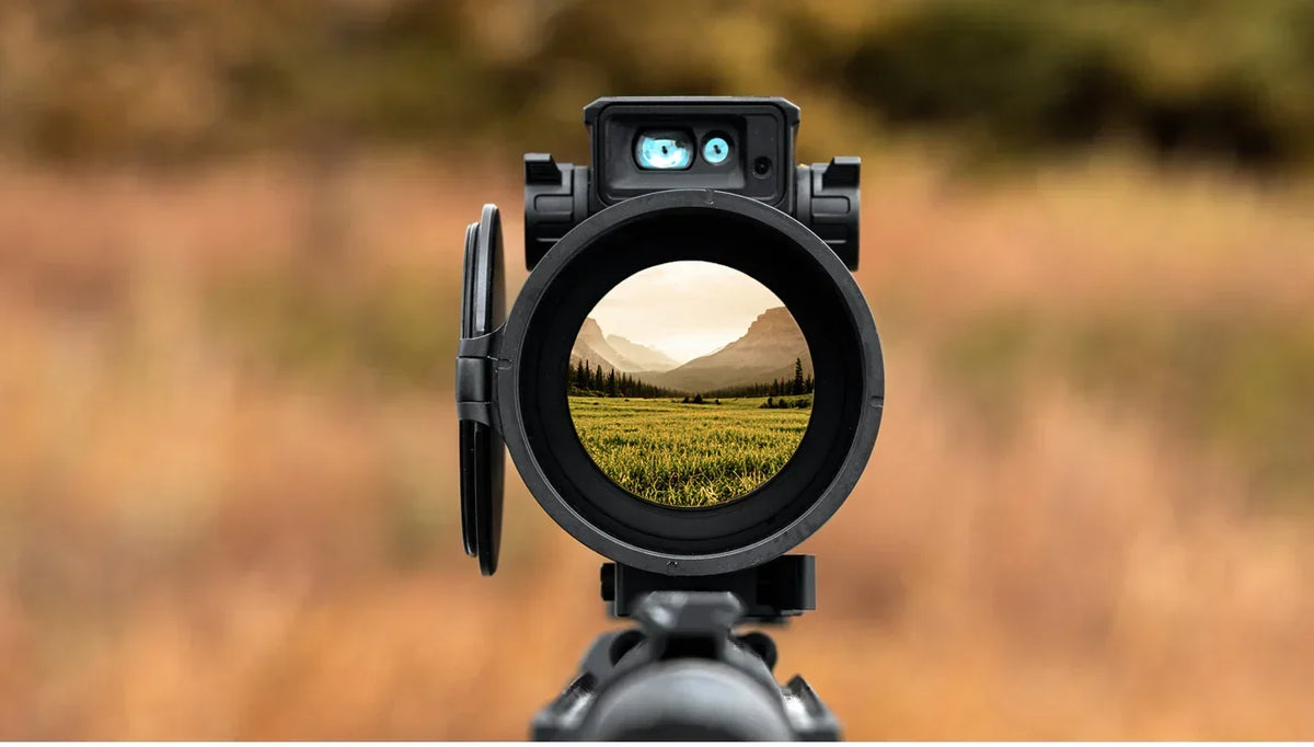 Close-up view of a digital night vision scope showing a landscape through the lens