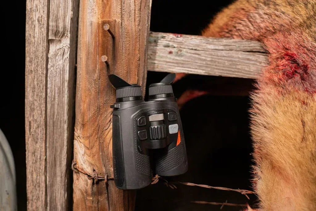 Thermal binoculars with buttons and eyepieces on rustic wooden fence, outdoor setting