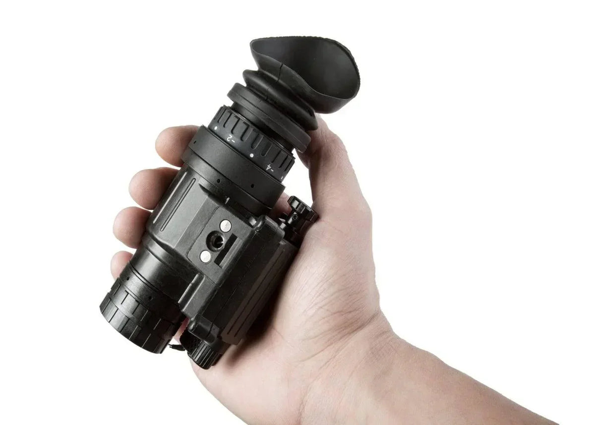 Hand holding a black night vision monocular device against a white background