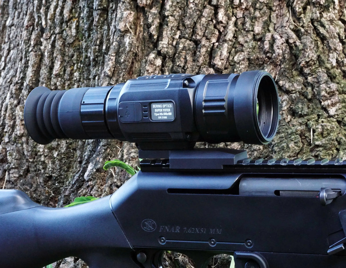 Thermal rifle scope with 25mm lens mounted on a rifle near tree bark outdoors