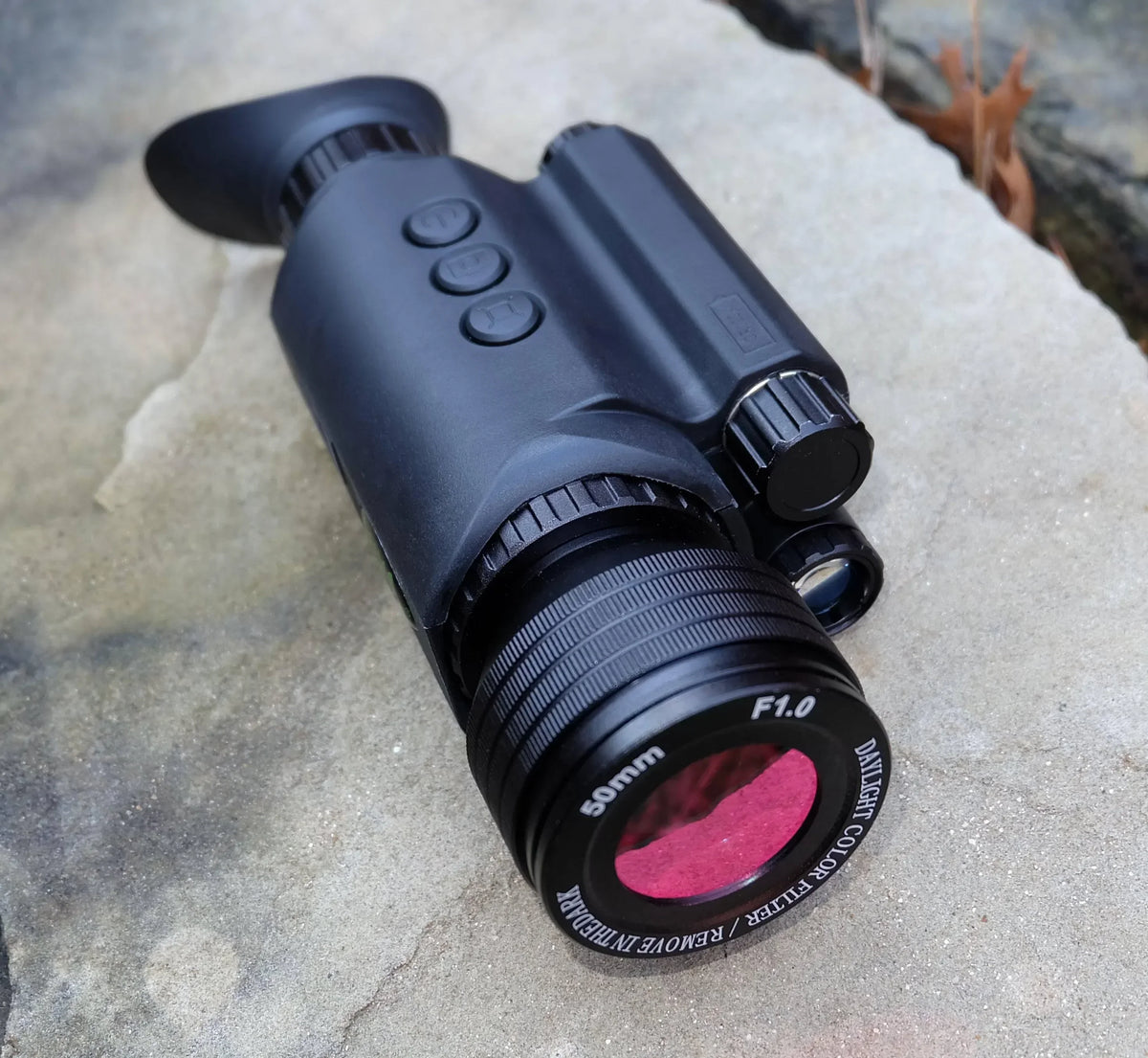 Digital day night monocular with 50mm lens and control buttons on stone surface